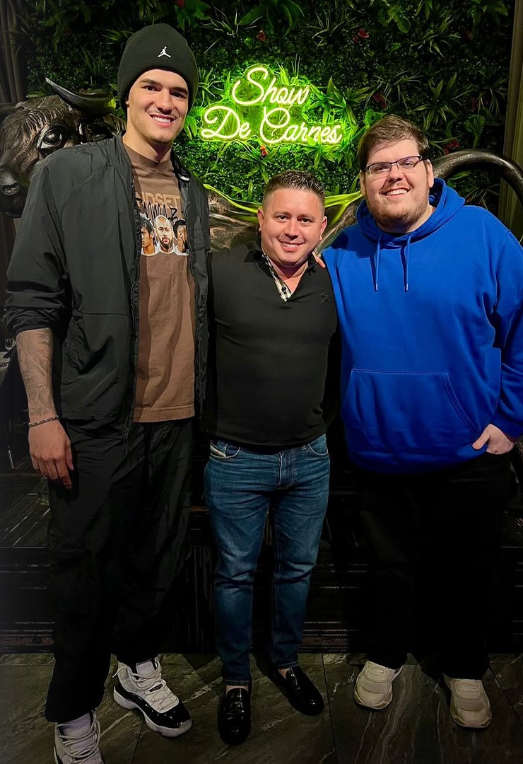 Celso, Gui Santos, and a friend posing together in a restaurant under the Show de Carnes neon sign.
